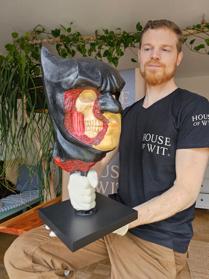 “House of Wit Batman anatomical bust, three-quarter view with exposed skull and red muscle on right side of face.”