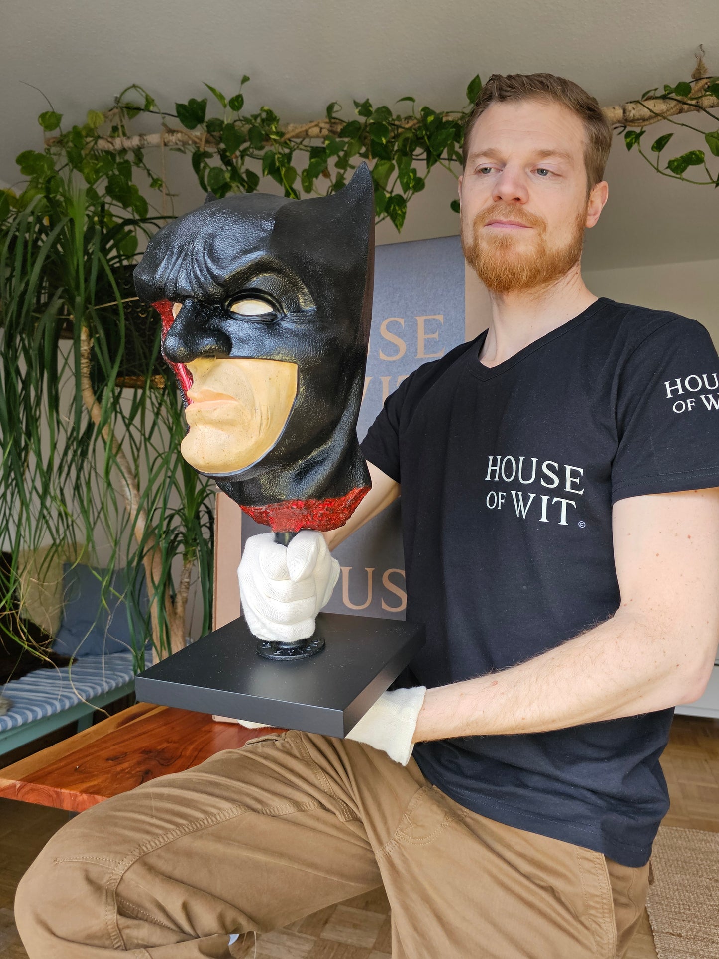 Artist holding bat-themed anatomical mask sculpture to show scale