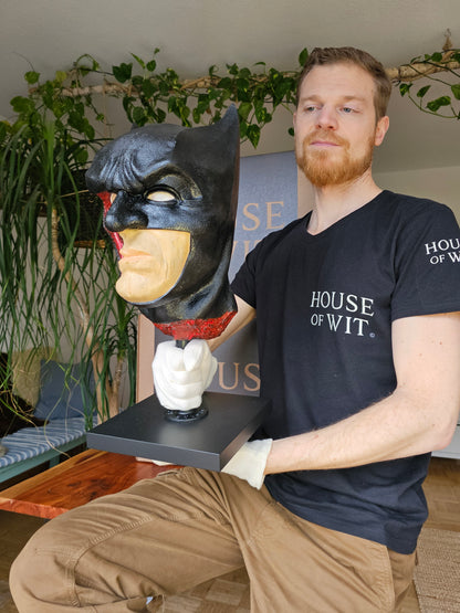 Artist holding bat-themed anatomical mask sculpture to show scale
